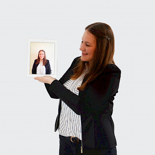 Porträt von V. Gornitzka, Steuerfachangestellte in dem Steuerbüro Clemens steht lächelnd im Anzug mit eine Bild von sich in der Hand.